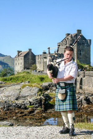 Bagpiper, Eileen Donan Castle in Dornie with Loch Duich, Scotlan